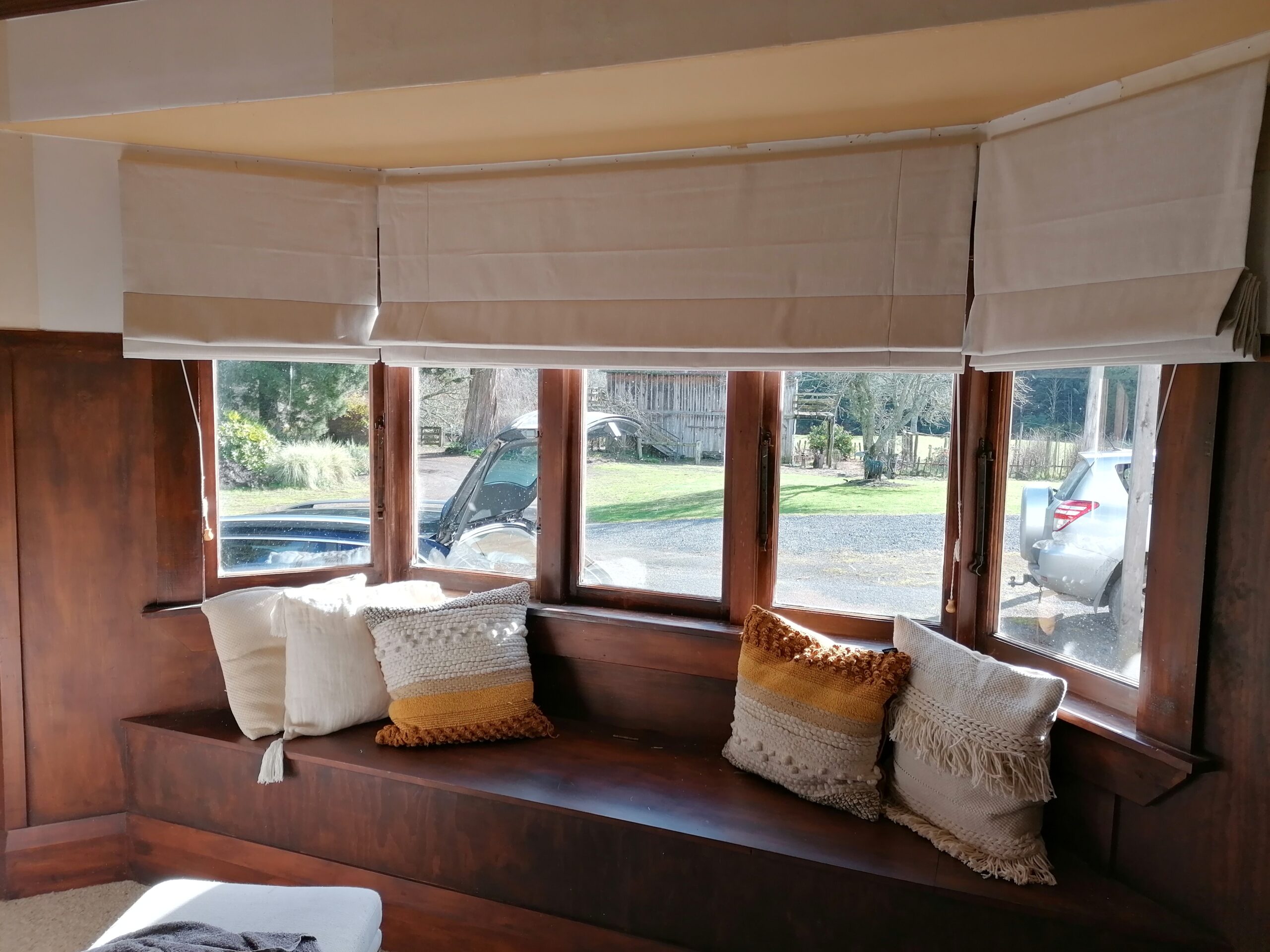 Bay window with custom Roman blind and neutral cushions on built-in window seat.